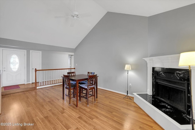 dining room featuring a fireplace with raised hearth, wood finished floors, baseboards, and ceiling fan