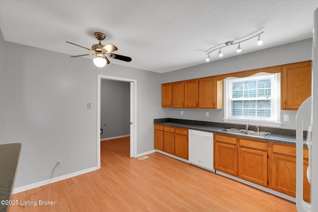 kitchen featuring light wood finished floors, a sink, dark countertops, brown cabinetry, and white dishwasher