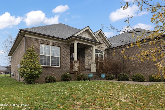 view of front of home with a front yard, brick siding, stone siding, and a shingled roof