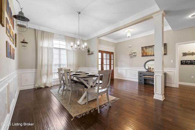 dining room with dark wood-style floors, ornate columns, ornamental molding, wainscoting, and a decorative wall