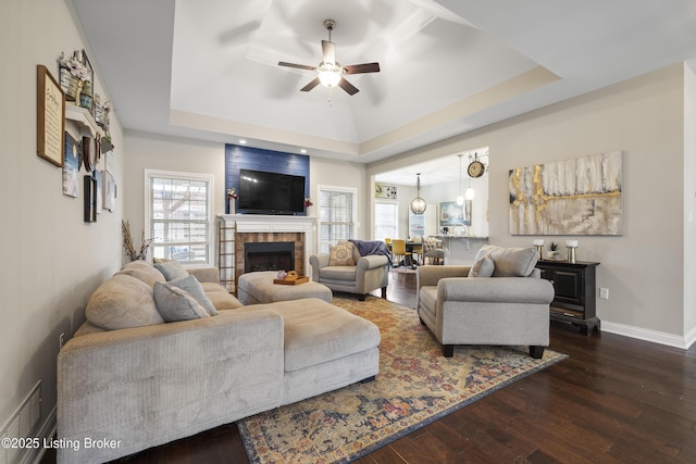 living room with a tray ceiling, baseboards, wood finished floors, and a ceiling fan