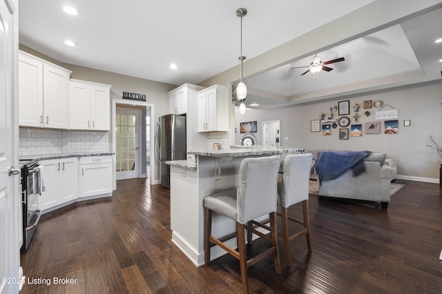 kitchen with a kitchen bar, open floor plan, stainless steel appliances, a peninsula, and a raised ceiling