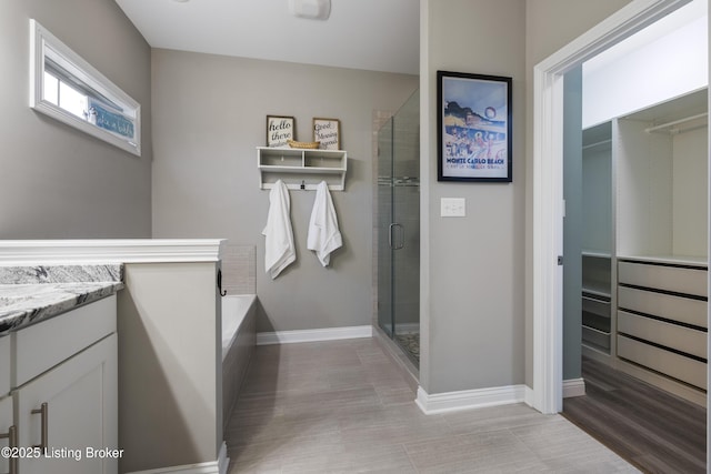 bathroom featuring a spacious closet, baseboards, a garden tub, a stall shower, and vanity