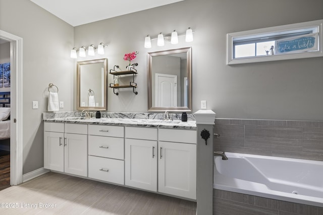 ensuite bathroom with double vanity, a bath, connected bathroom, and a sink