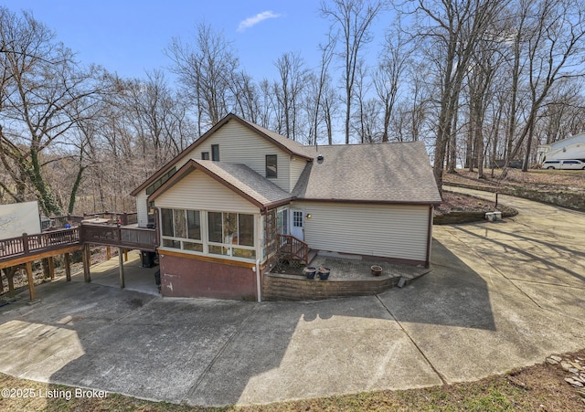 rear view of house featuring a deck, driveway, roof with shingles, and a sunroom