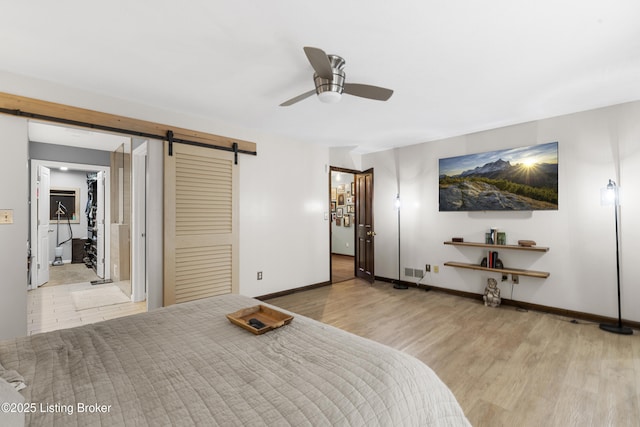 bedroom featuring wood finished floors, a barn door, baseboards, ceiling fan, and a spacious closet