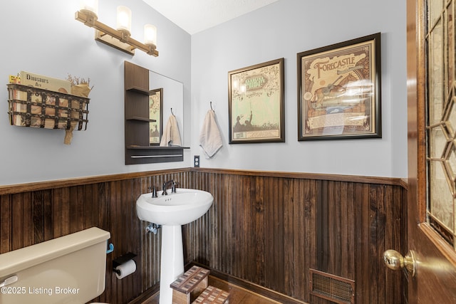 half bath with wooden walls, toilet, and a wainscoted wall