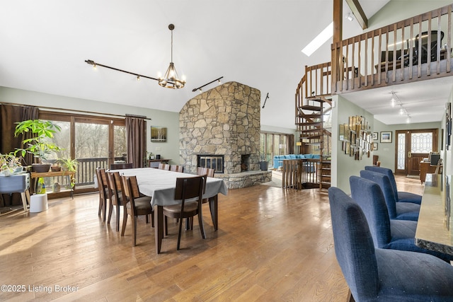 dining space featuring stairway, a stone fireplace, wood finished floors, a notable chandelier, and high vaulted ceiling