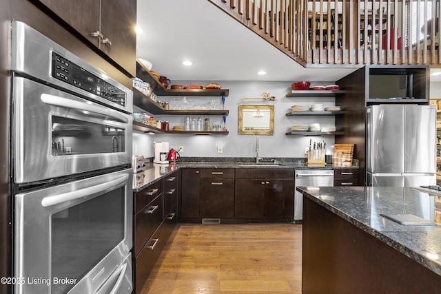 kitchen featuring light wood finished floors, a sink, stainless steel appliances, and open shelves