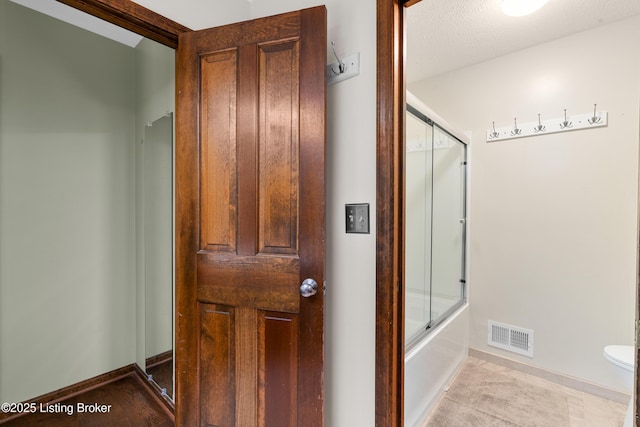 bathroom with combined bath / shower with glass door, visible vents, baseboards, and toilet