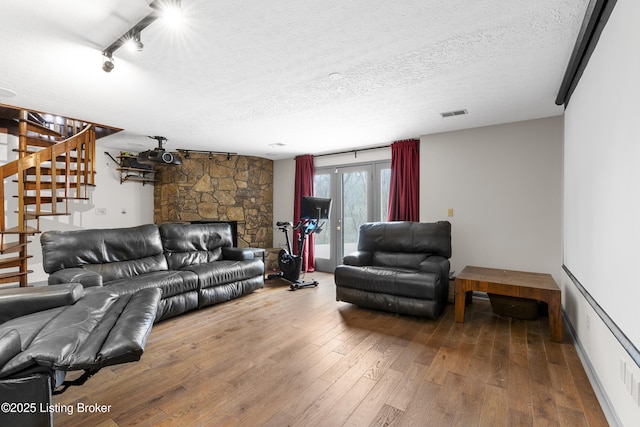 living area with stairway, a textured ceiling, visible vents, and hardwood / wood-style flooring