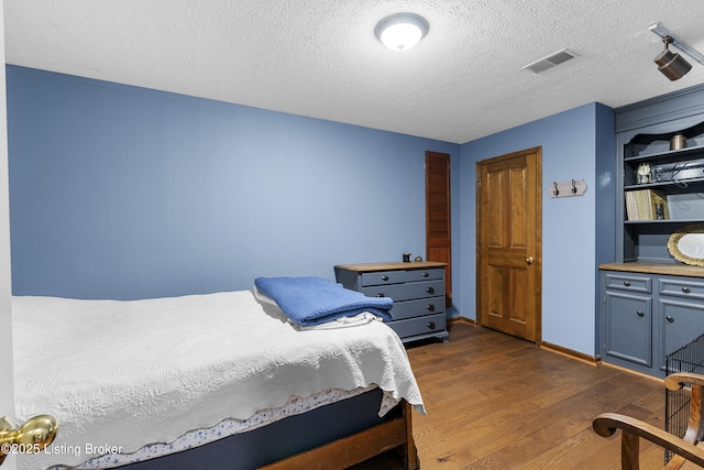 bedroom featuring dark wood-type flooring, baseboards, visible vents, and a textured ceiling