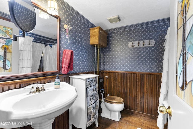 bathroom with wallpapered walls, wood finished floors, a wainscoted wall, and a sink