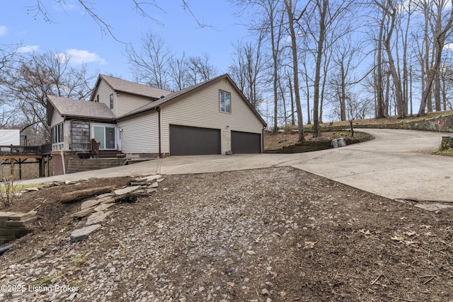 view of side of property featuring concrete driveway, a garage, and roof with shingles