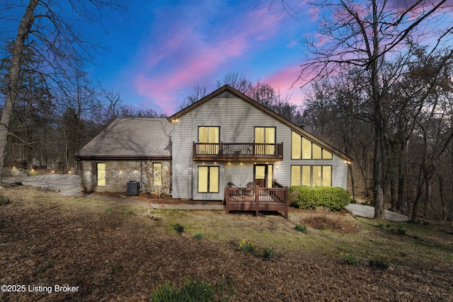 back of house at dusk featuring a wooden deck, central AC, and a balcony