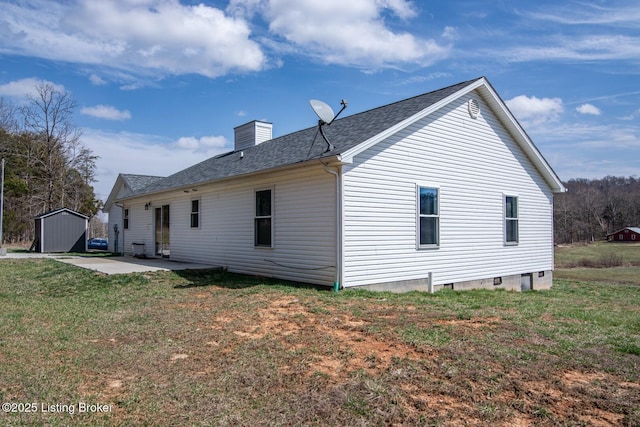 back of house featuring an outbuilding, a lawn, a shed, a chimney, and a patio area