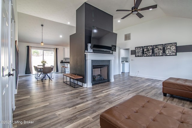 living area with visible vents, high vaulted ceiling, a ceiling fan, wood finished floors, and baseboards