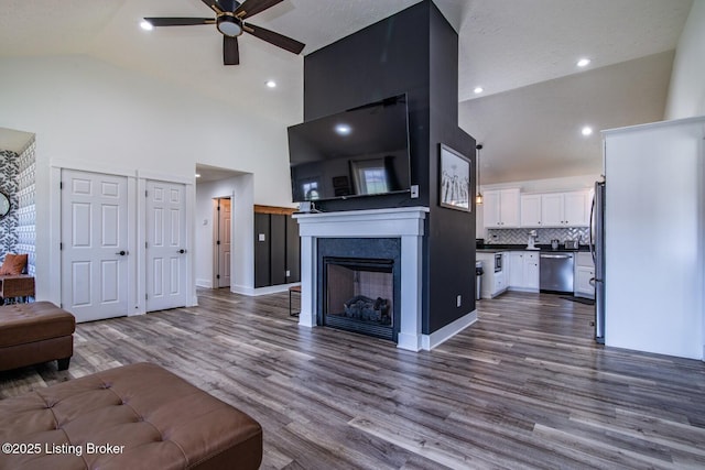 living area featuring baseboards, a ceiling fan, dark wood-style flooring, and high vaulted ceiling