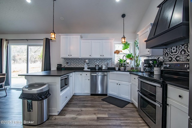 kitchen with dark countertops, custom range hood, a peninsula, stainless steel appliances, and white cabinetry