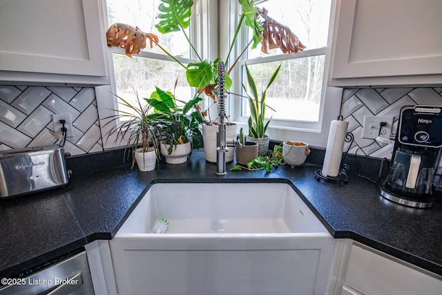 room details featuring decorative backsplash, dark countertops, white cabinets, and stainless steel dishwasher