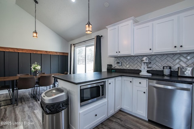 kitchen with dark countertops, dark wood-type flooring, lofted ceiling, appliances with stainless steel finishes, and white cabinetry