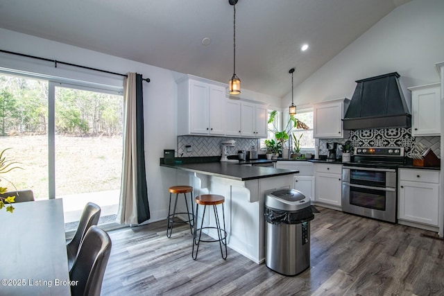 kitchen with double oven range, white cabinetry, dark countertops, and custom range hood