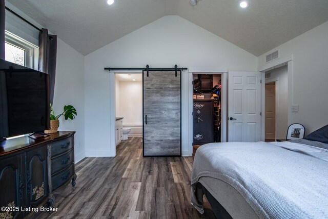 bedroom with visible vents, wood finished floors, a barn door, a spacious closet, and vaulted ceiling