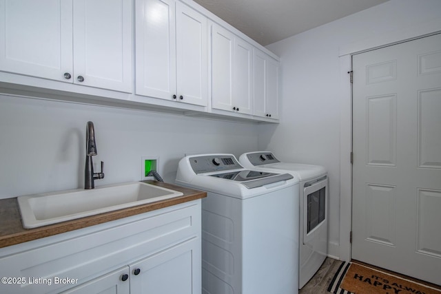 clothes washing area featuring wood finished floors, washing machine and dryer, cabinet space, and a sink