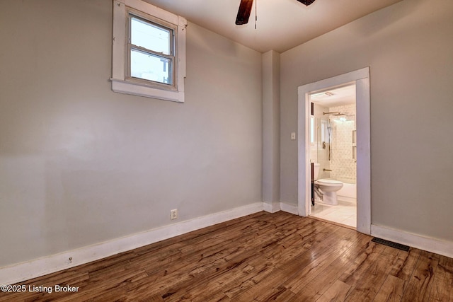 spare room with hardwood / wood-style flooring, a ceiling fan, visible vents, and baseboards