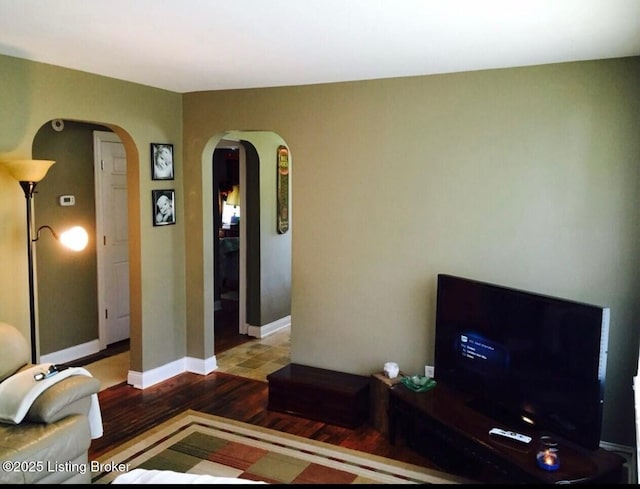 living room featuring arched walkways, baseboards, and wood finished floors