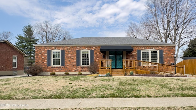 view of front of home featuring brick siding, roof with shingles, a front yard, and fence