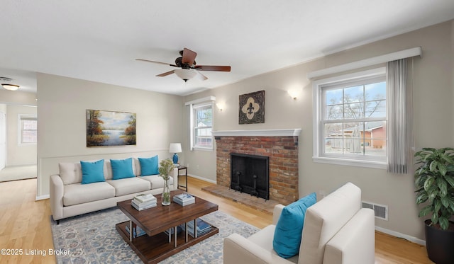 living area with visible vents, light wood-style floors, a fireplace, baseboards, and ceiling fan