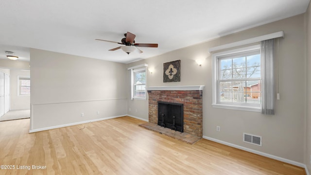 unfurnished living room with a ceiling fan, wood finished floors, visible vents, and a fireplace