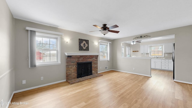 unfurnished living room featuring baseboards, light wood-style floors, a brick fireplace, and a ceiling fan