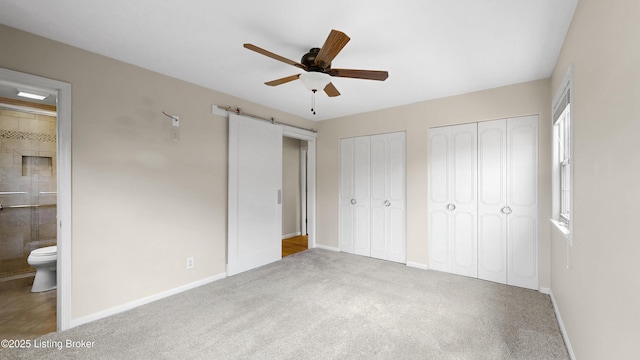 unfurnished bedroom with baseboards, multiple closets, a barn door, carpet floors, and ensuite bathroom