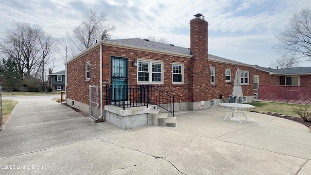 rear view of house featuring driveway, a patio, fence, brick siding, and a chimney