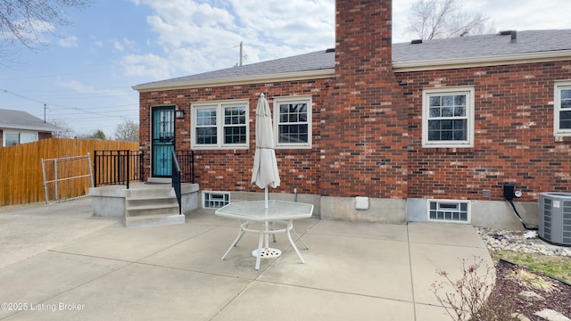 back of house featuring a patio, fence, a chimney, central air condition unit, and brick siding