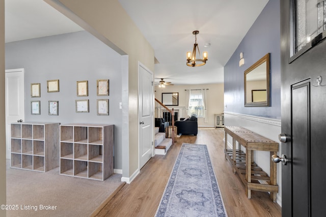 foyer entrance with ceiling fan with notable chandelier, stairs, baseboards, and wood finished floors