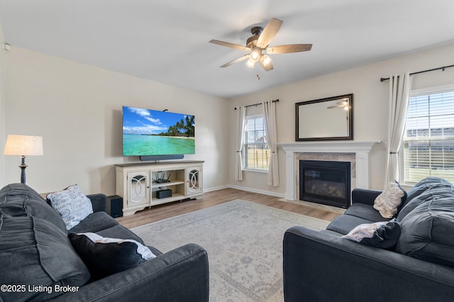 living area with a fireplace with flush hearth, baseboards, a ceiling fan, and wood finished floors