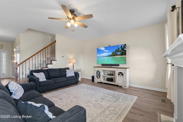 living room with wood finished floors, visible vents, baseboards, ceiling fan, and stairs