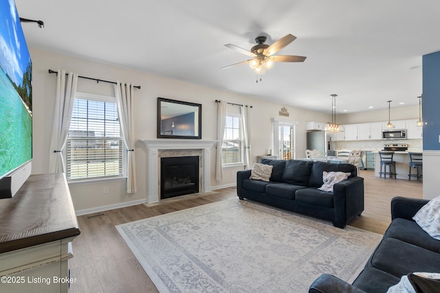 living room with baseboards, light wood-type flooring, a high end fireplace, and ceiling fan