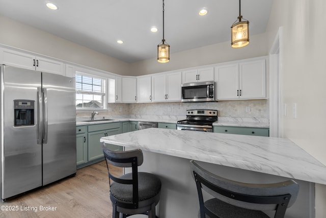 kitchen featuring a sink, tasteful backsplash, white cabinetry, stainless steel appliances, and a breakfast bar area