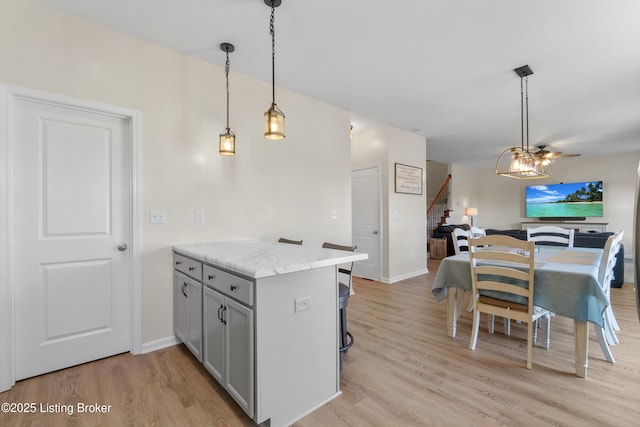 kitchen featuring baseboards, a breakfast bar, gray cabinets, light wood-style floors, and hanging light fixtures