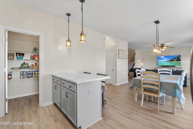 kitchen with hanging light fixtures, light stone counters, light wood finished floors, and gray cabinetry