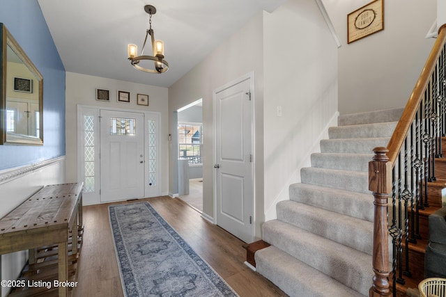 foyer entrance with baseboards, stairs, an inviting chandelier, and wood finished floors