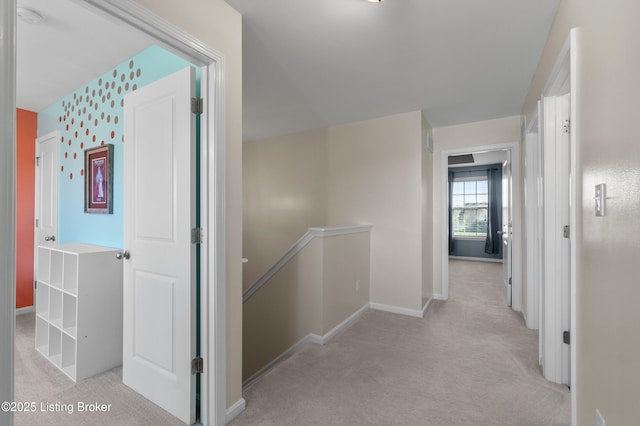 hallway featuring an upstairs landing, light carpet, and baseboards