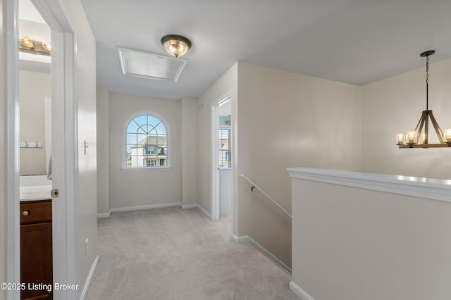 hallway with an upstairs landing, an inviting chandelier, baseboards, light colored carpet, and attic access