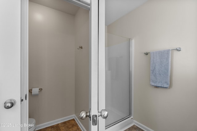 bathroom with baseboards, toilet, and a stall shower