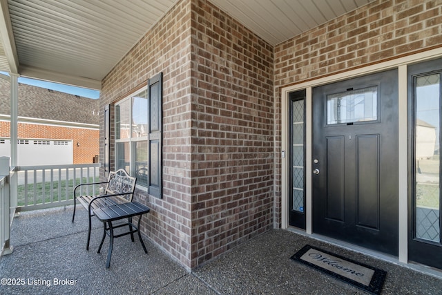 view of exterior entry with a porch and brick siding