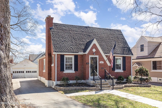 tudor home with an outbuilding, a shingled roof, a chimney, a detached garage, and brick siding